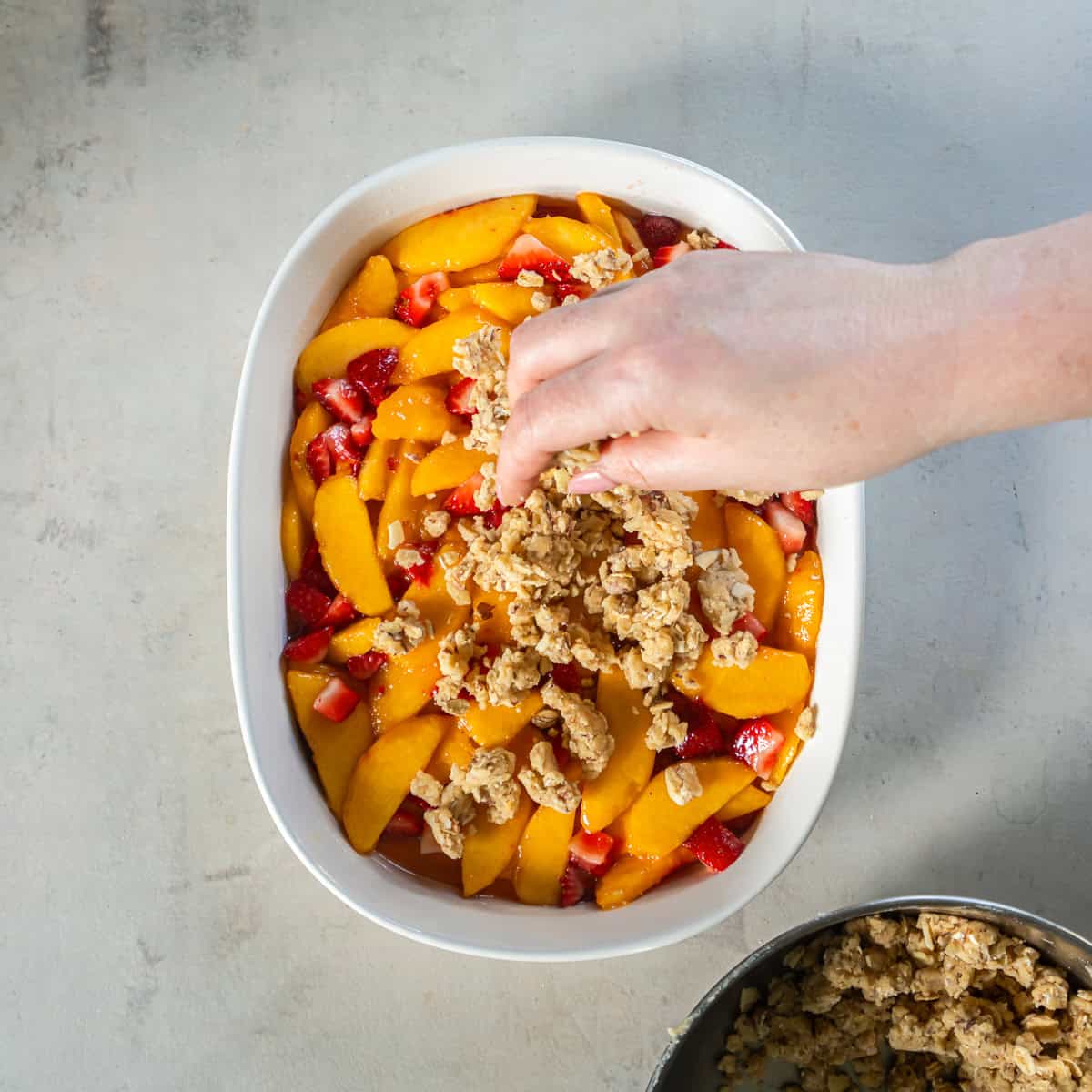 Sprinkling the crisp topping evenly over the peach and strawberry filling.