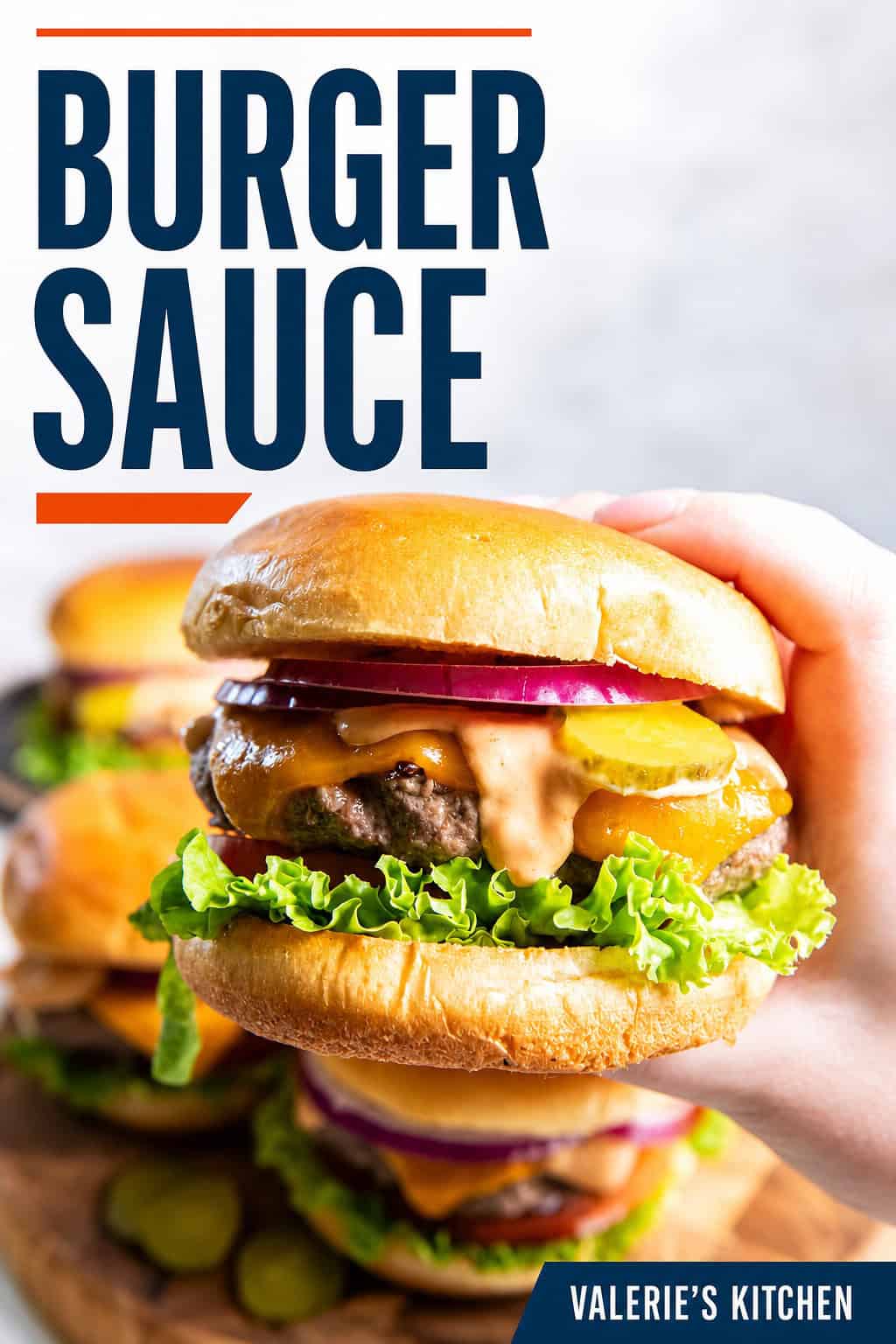Hand holding a cheeseburger topped with homemade burger sauce, cheddar cheese, pickles, red onion, lettuce, and tomato with bold text overlay.