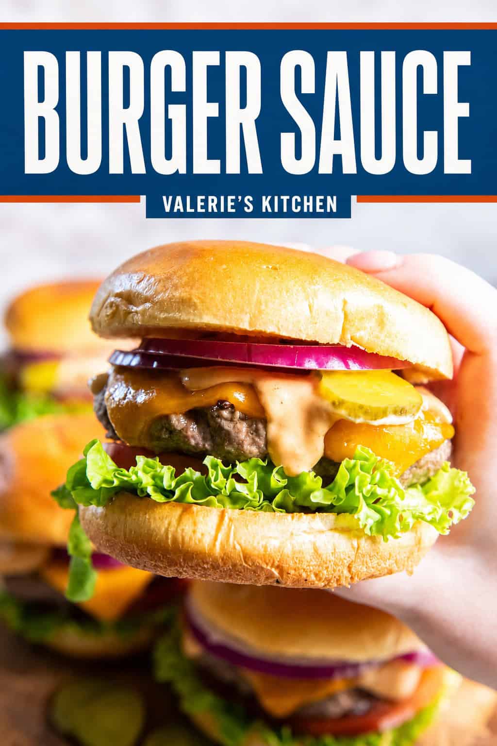 Hand holding a cheeseburger topped with homemade burger sauce, cheddar cheese, pickles, red onion, lettuce, and tomato with bold text overlay.