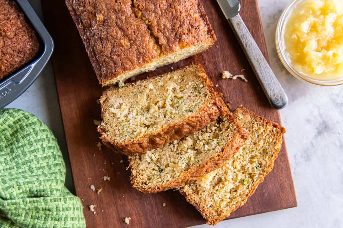 A loaf of Pineapple Zucchini Bread with several slices on a wooden cutting board.