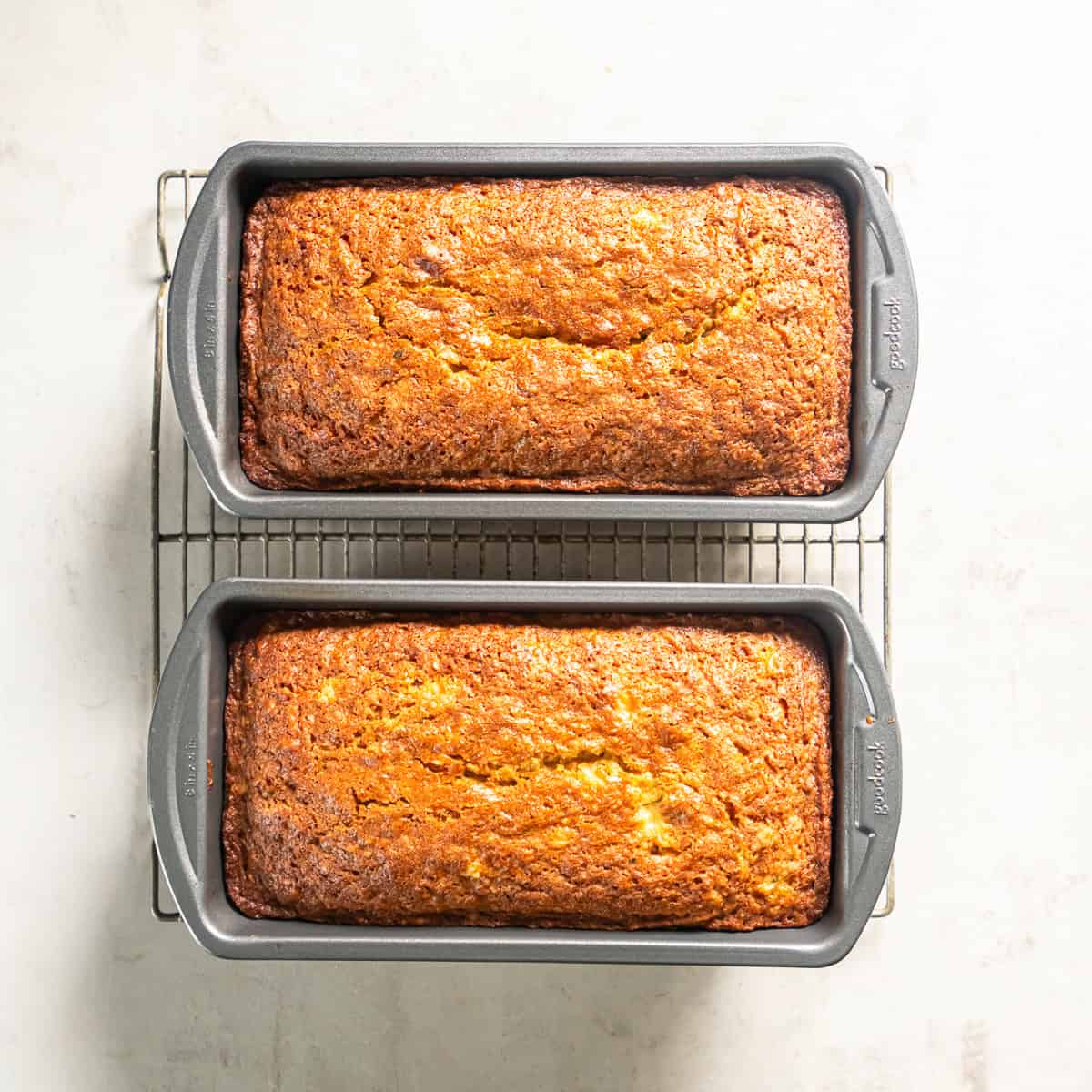 Two freshly baked loaves of Pineapple Zucchini Bread cooling in 8 x 4-inch loaf pans on a wire rack.