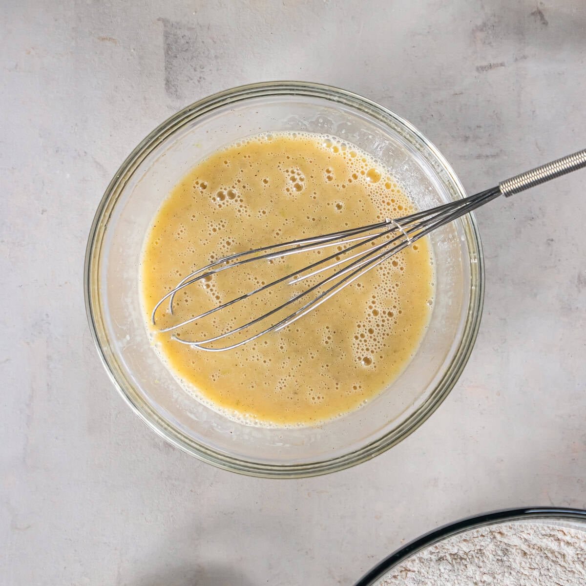 Whisked wet ingredients for Pineapple Zucchini Bread, including eggs, oil, vanilla, pineapple juice, and lime.
