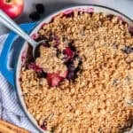 Apple Berry Crisp with a spoonful lifted from the baking dish, showing tender apples, berries, and a golden oat topping.