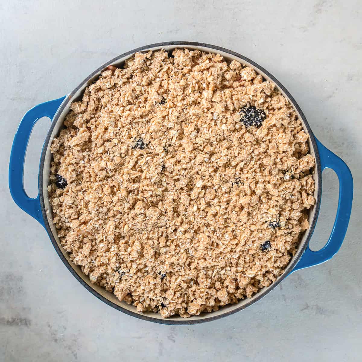 Apple berry filling covered evenly with a crumbly oat and cinnamon crisp topping before baking.