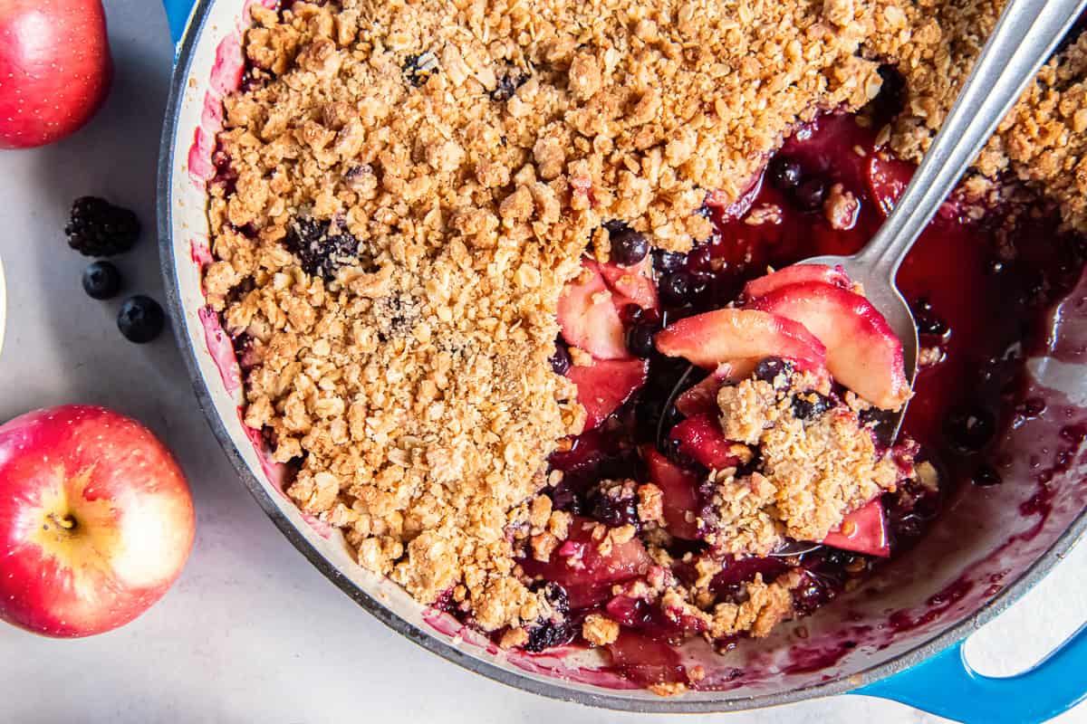 Apple Berry Crisp in a blue baking dish with a spoonful of tender apples and berries lifted through the golden oat topping.