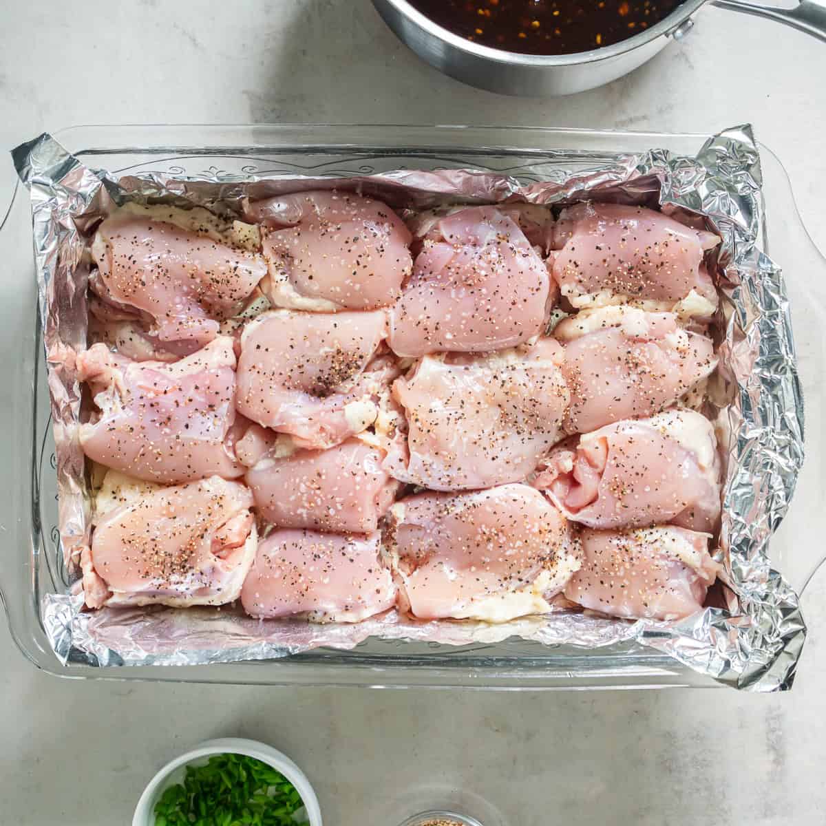 Boneless chicken thighs seasoned with salt and pepper in a foil-lined baking dish.