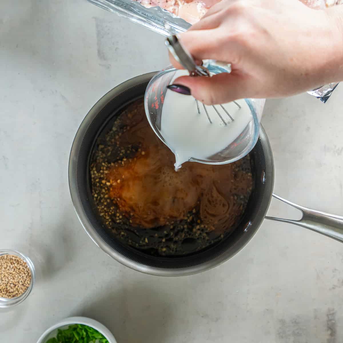 Cornstarch slurry being added to homemade teriyaki sauce in a saucepan.