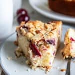 Slice of cherry coffee cake with fresh cherries and an almond streusel topping served with coffee.