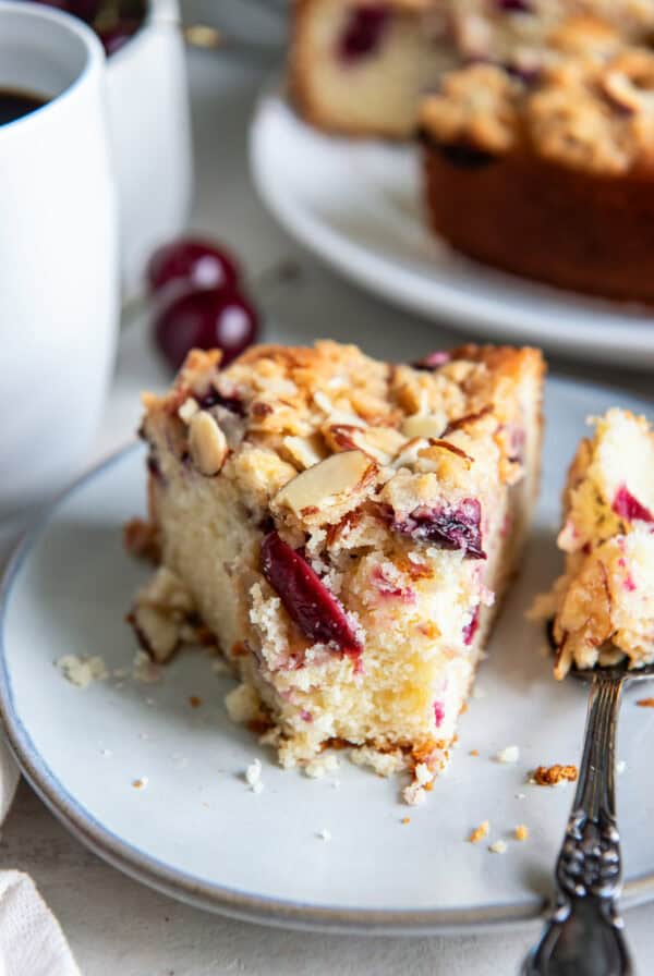 Slice of cherry coffee cake with fresh cherries and an almond streusel topping served with coffee.