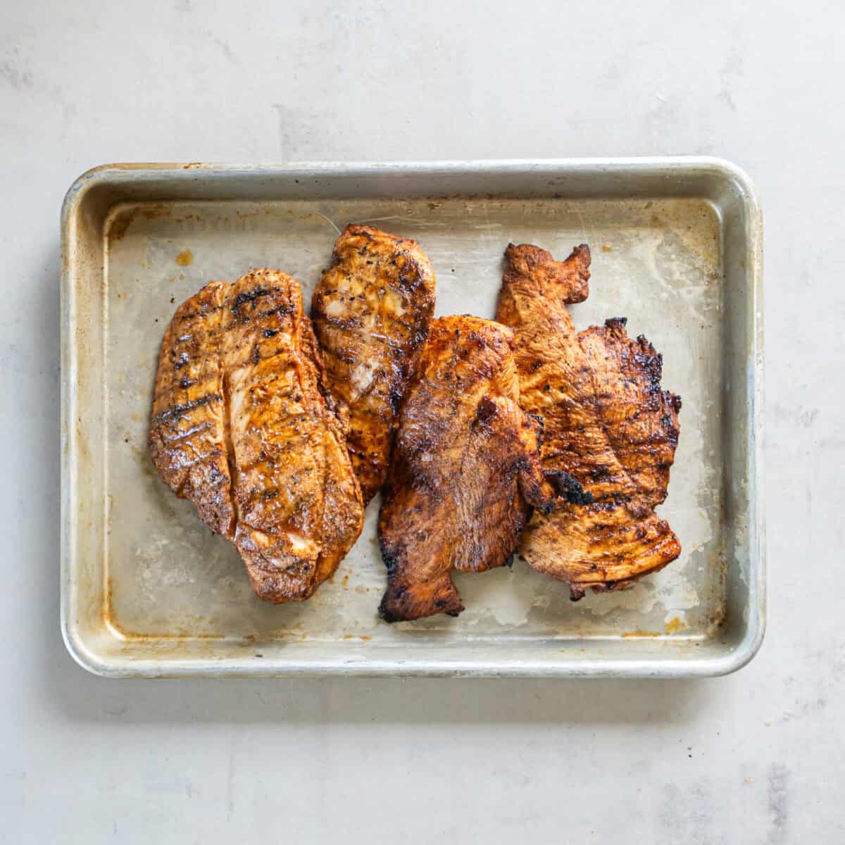 Grilled chili lime chicken breasts with browned edges and grill marks on a sheet pan.