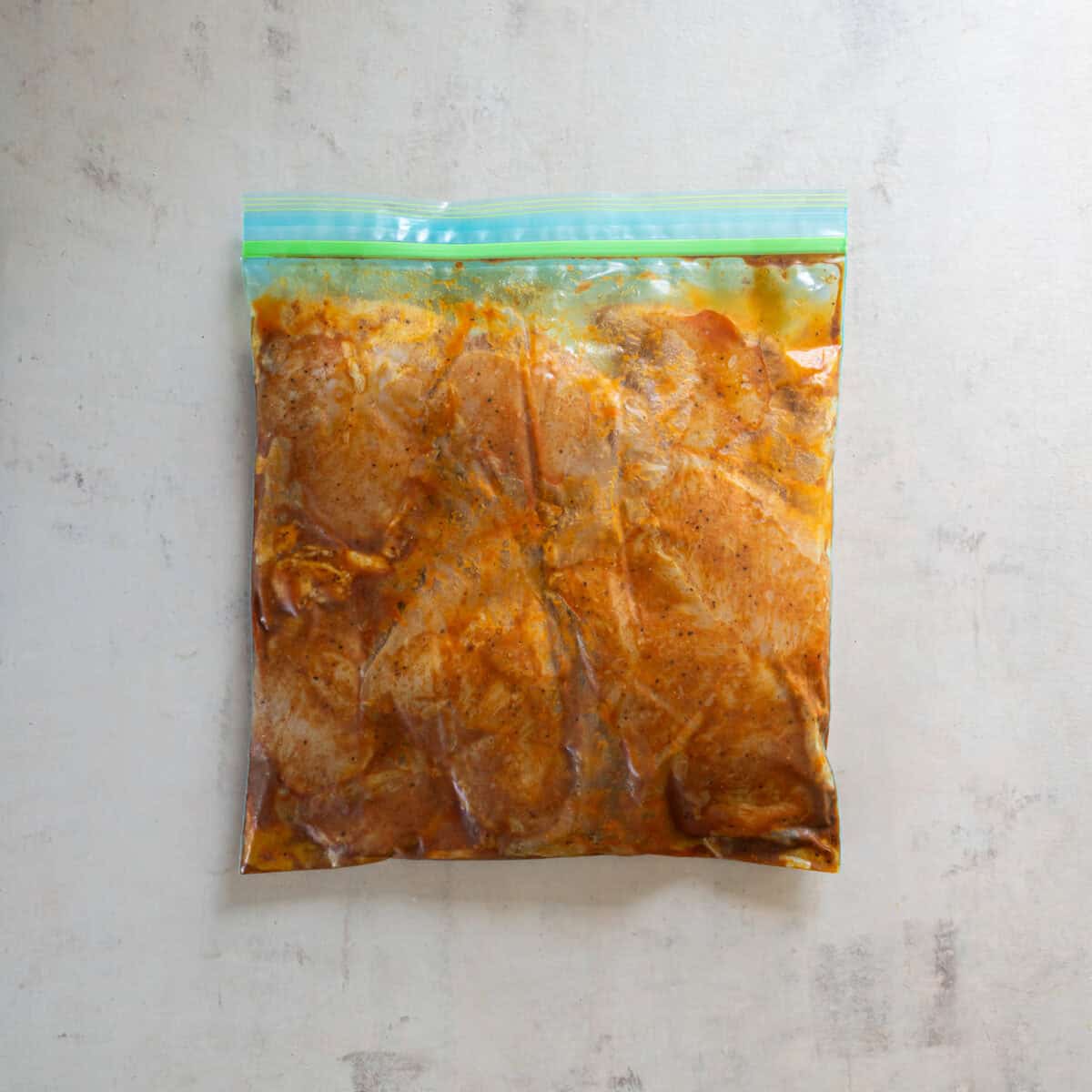 Chicken breasts coated in chili lime marinade in a sealed zip-top bag.