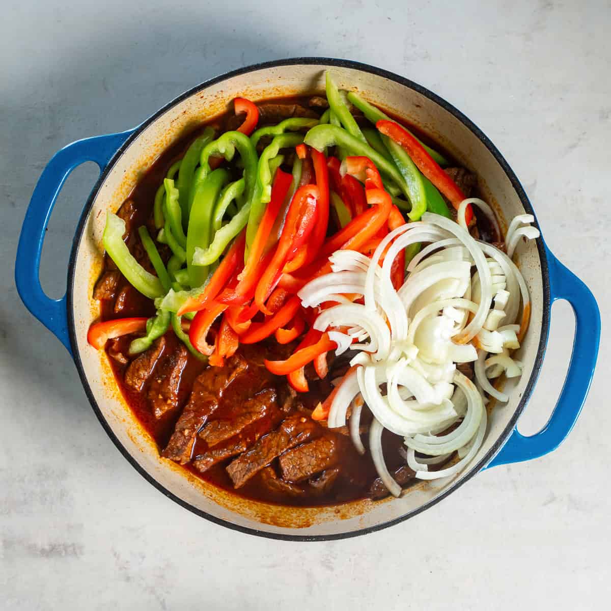 Sliced bell peppers and onion added to the simmering beef mixture.
