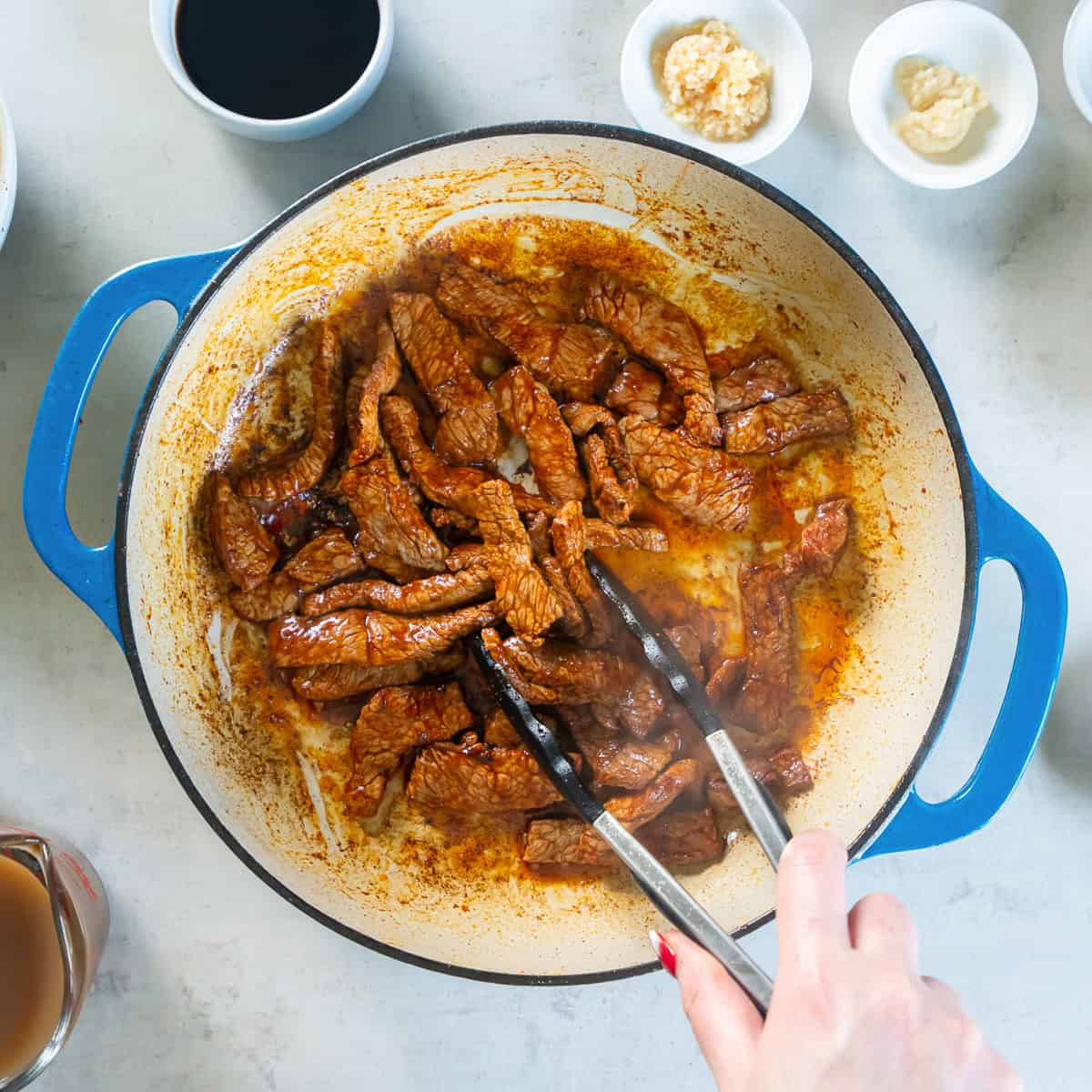 Thinly sliced beef browning in oil in a light-colored skillet.