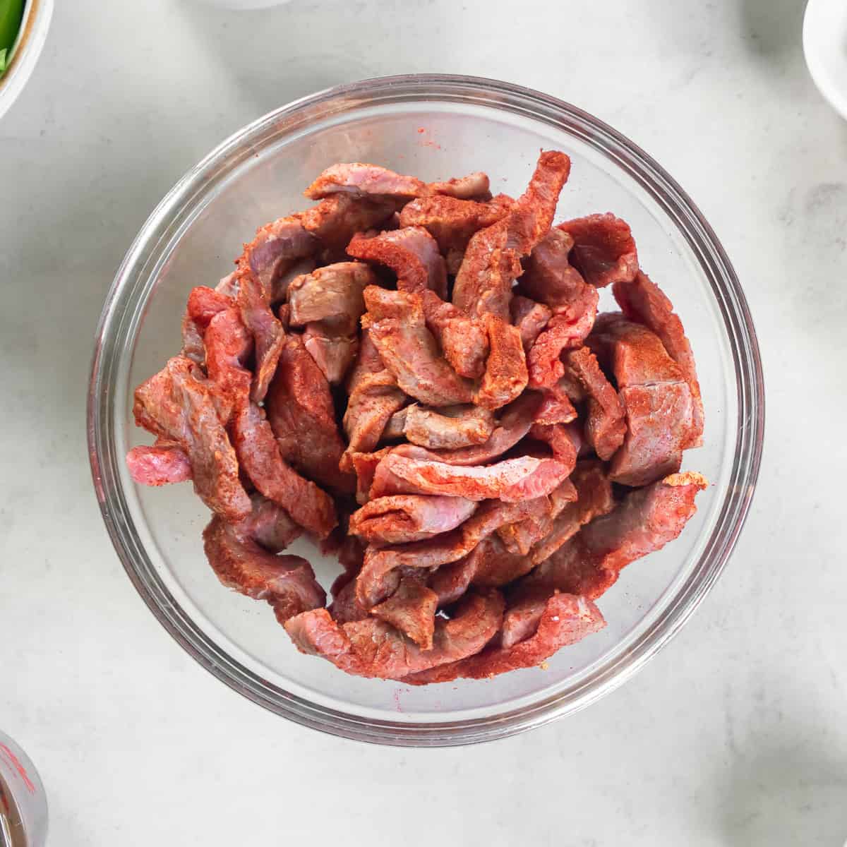 Thinly sliced beef tossed with paprika in a glass mixing bowl.