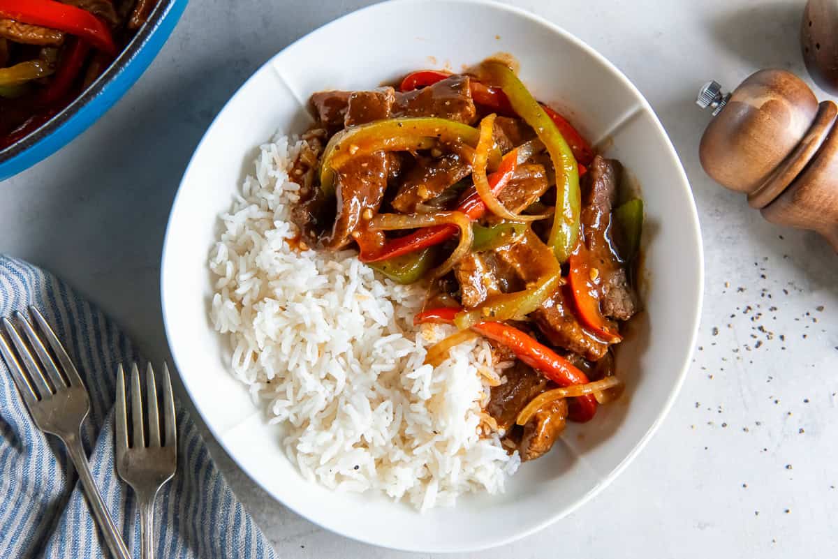 Bowl of classic pepper steak with tender beef strips, colorful bell peppers, onion, and savory brown sauce served over white rice.