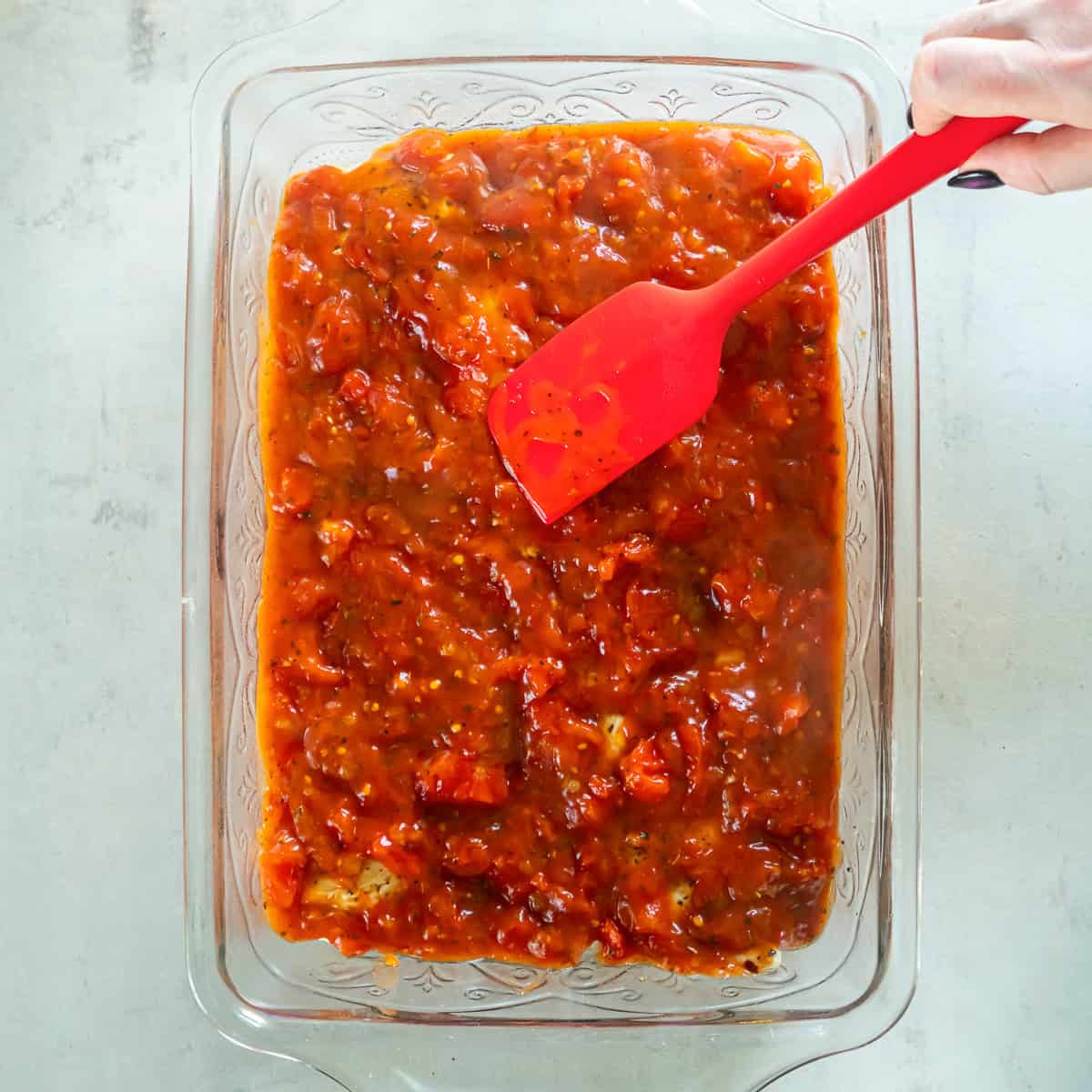 Adding dried basil, oregano, and red pepper flakes to the tomato sauce.
