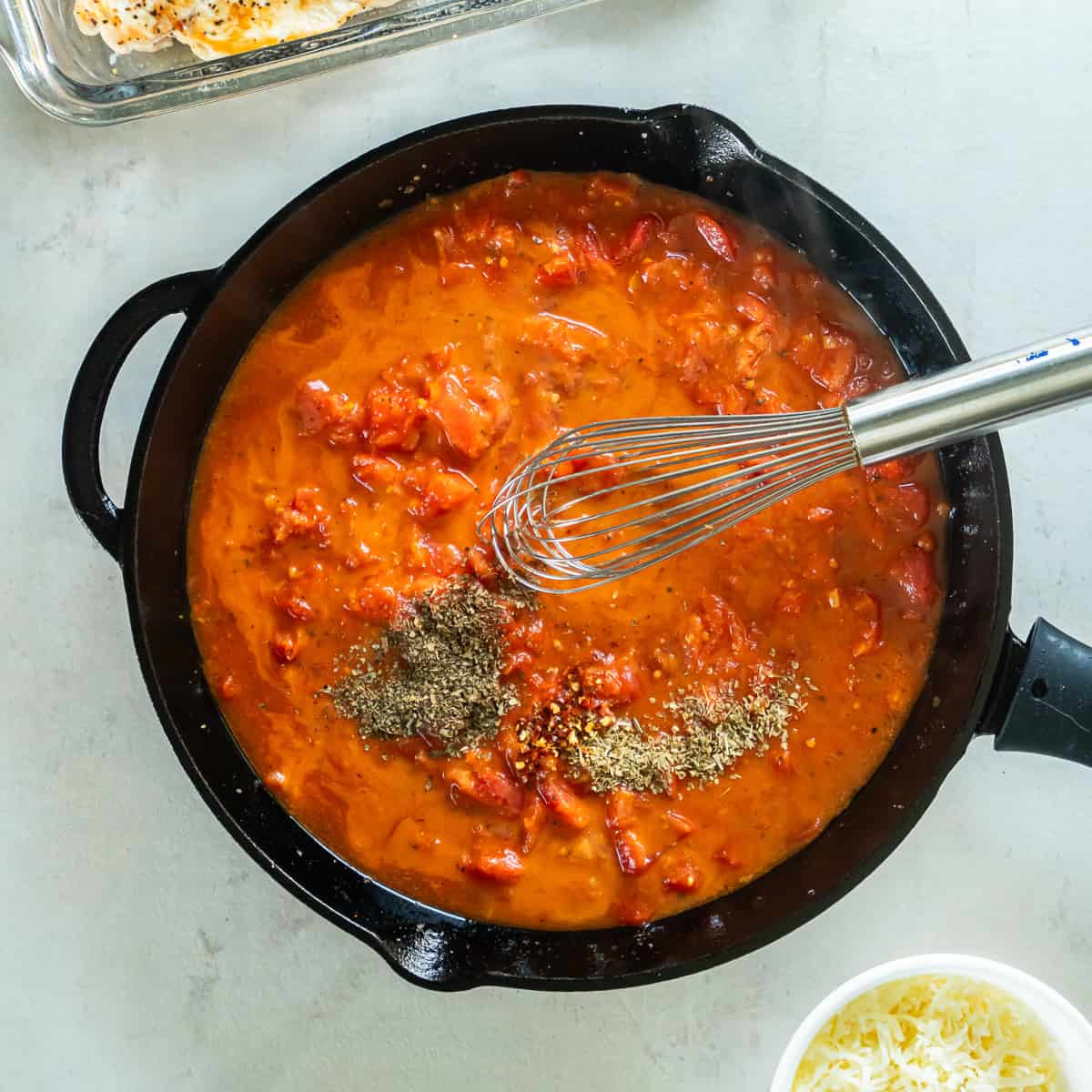 Adding dried basil, oregano, and red pepper flakes to the tomato sauce.