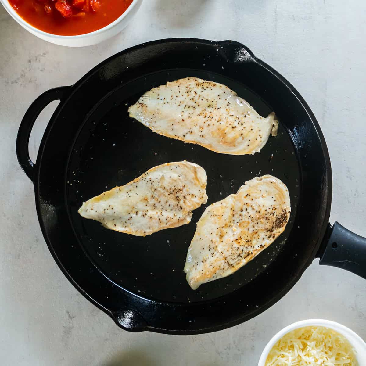 Seasoned chicken breasts browning in a skillet.