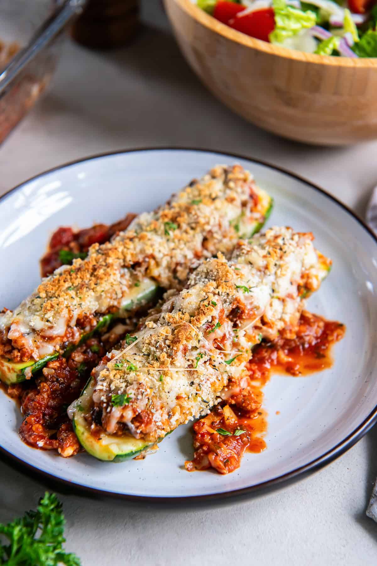 Italian stuffed zucchini boats topped with melted cheese and golden breadcrumbs, served with tomato meat sauce on a plate.