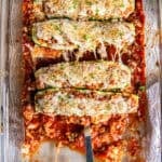 A spatula resting under an Italian Stuffed Zucchini Boat in a baking dish.