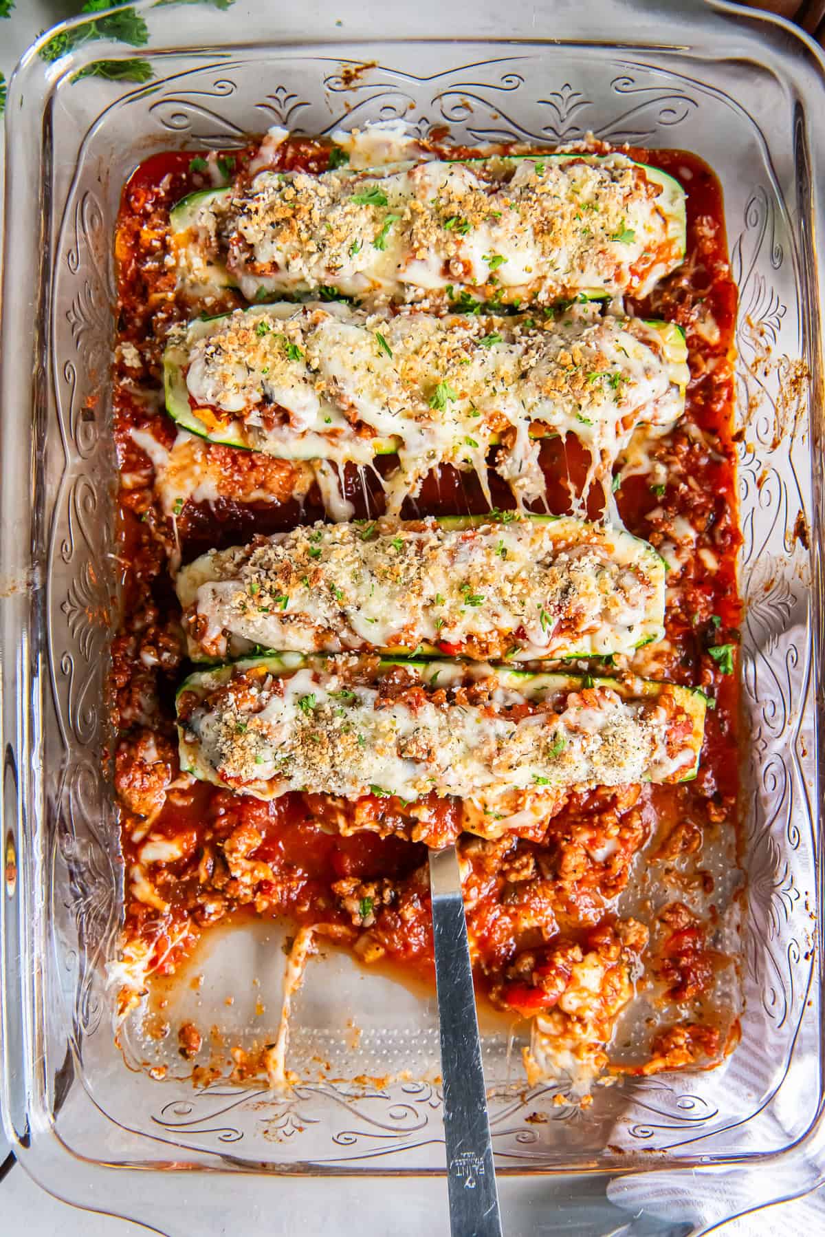 A spatula resting under an Italian Stuffed Zucchini Boat in a baking dish.
