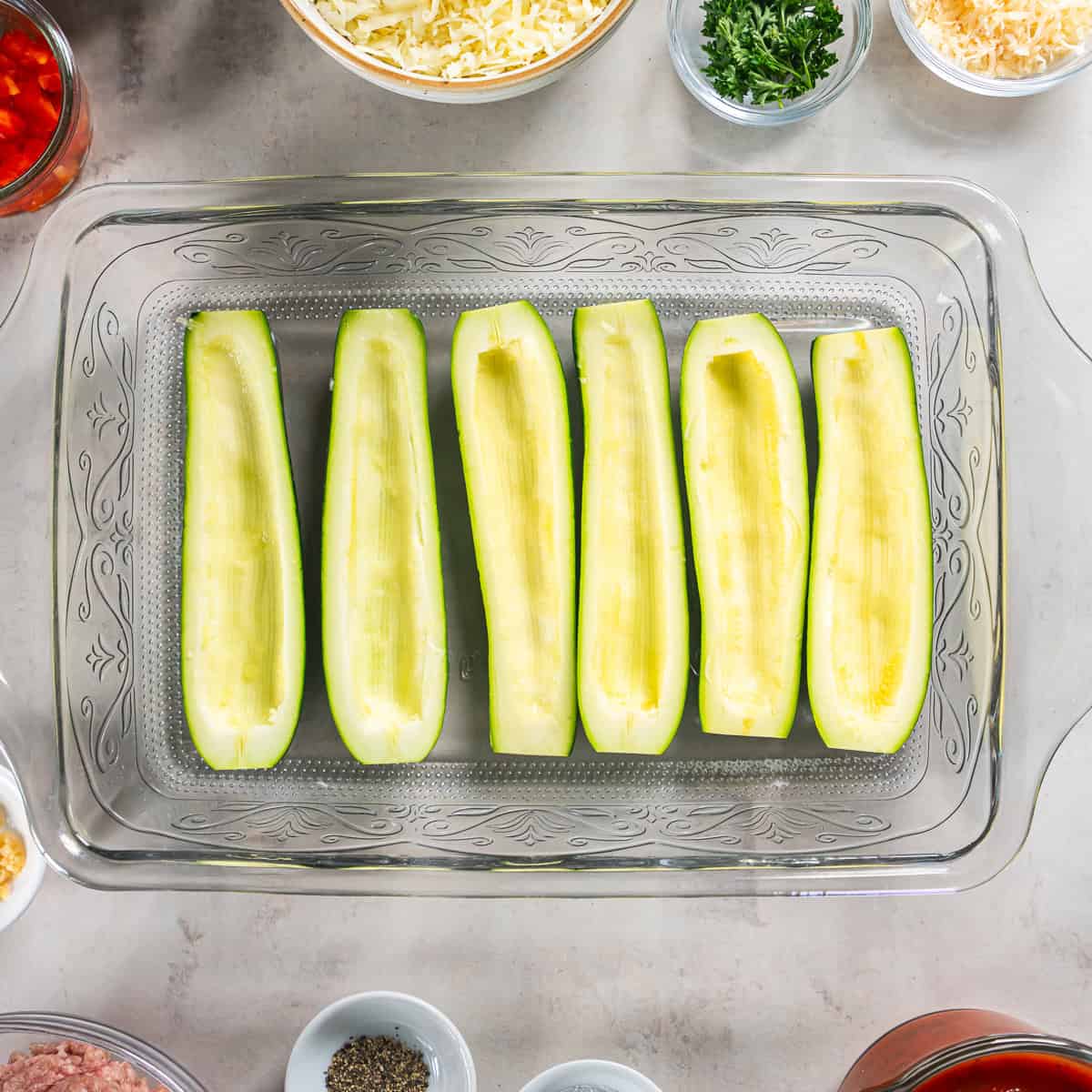 Hollowed zucchini boats arranged in a baking dish with water.