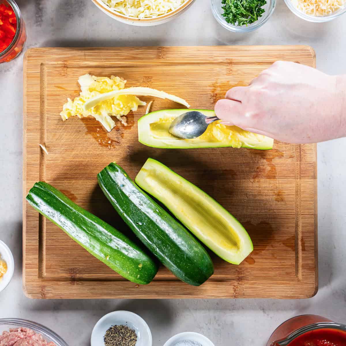 Scooping the flesh from zucchini halves with a spoon to create zucchini boats.