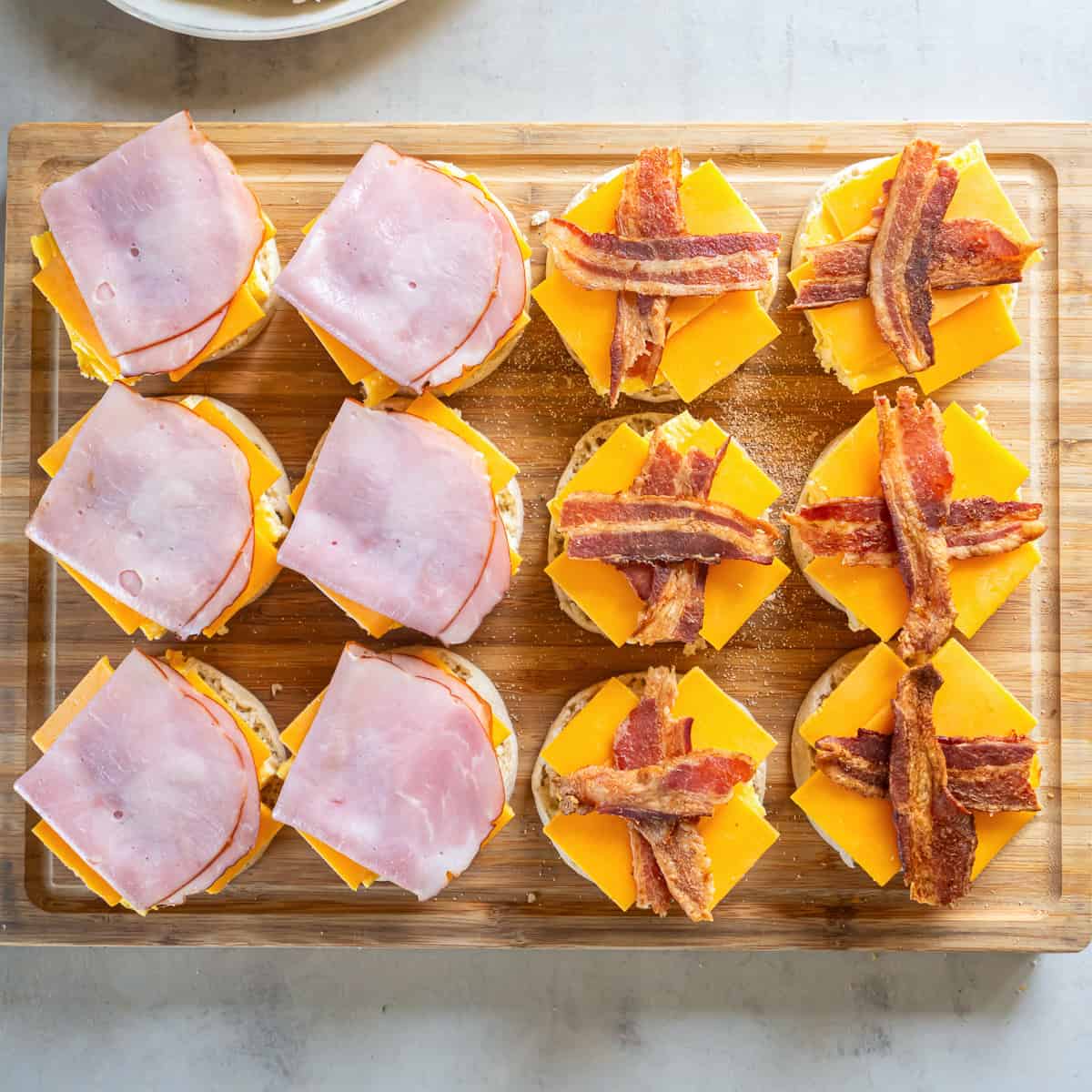 Breakfast sandwiches topped with folded deli ham or crisscrossed bacon over the egg and cheddar cheese.