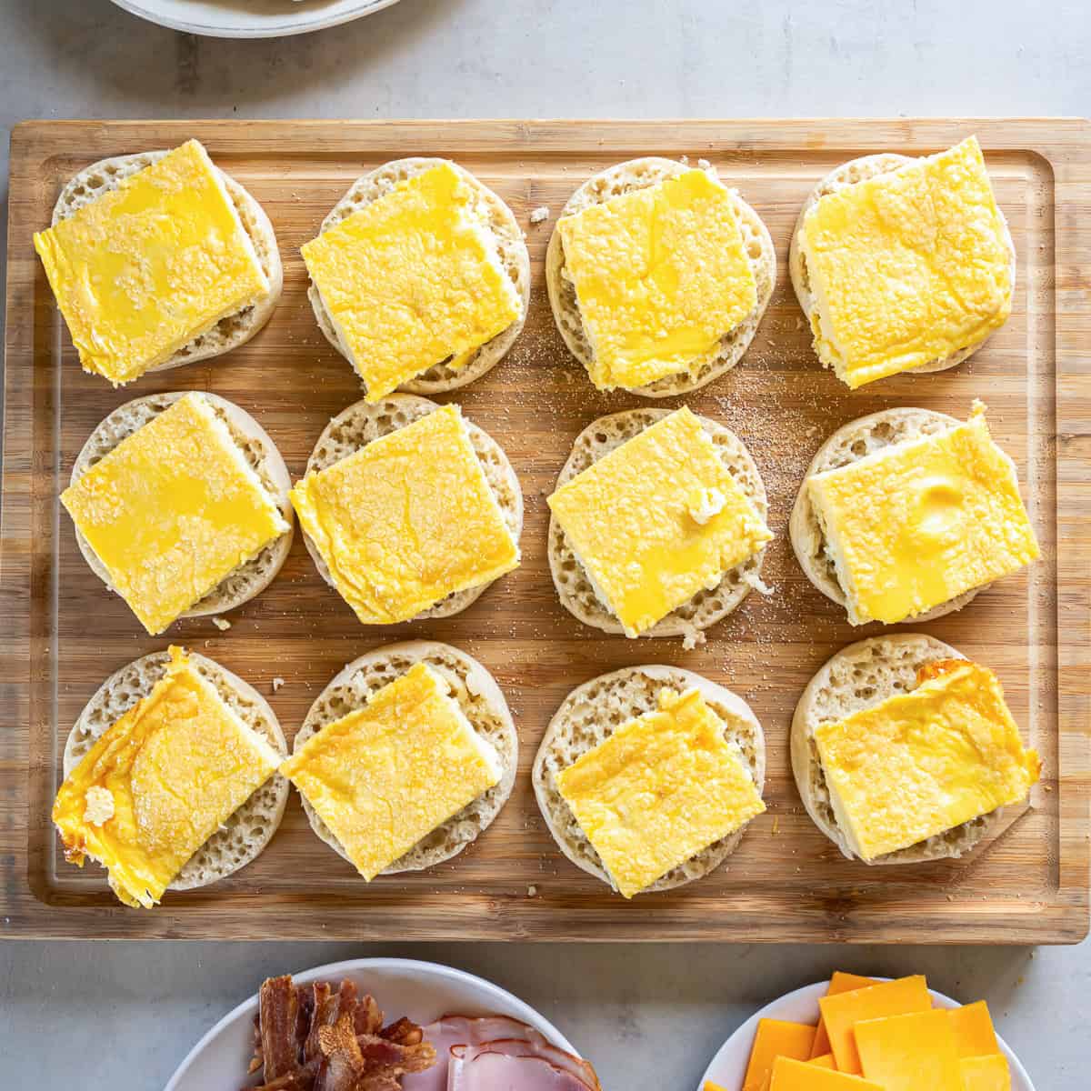 Egg squares arranged on the bottom halves of 12 English muffins for make-ahead breakfast sandwiches.