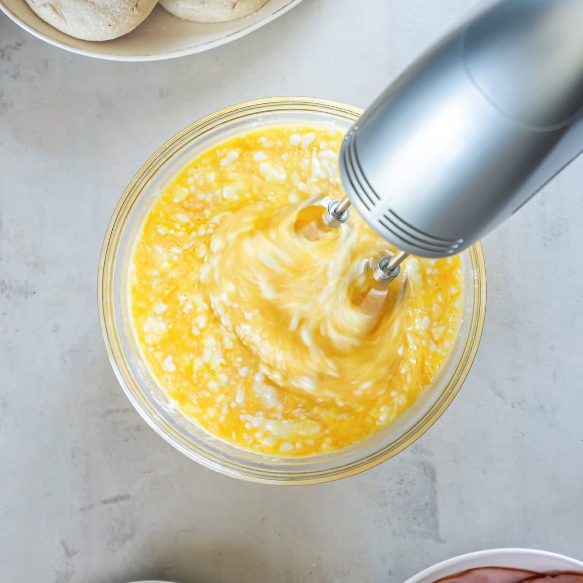 Eggs and cottage cheese being combined with a hand mixer in a glass mixing bowl.