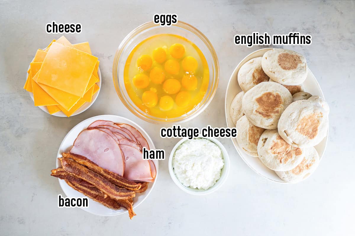Ingredients for make-ahead breakfast sandwiches including eggs, cottage cheese, English muffins, cheddar cheese, ham, and bacon.