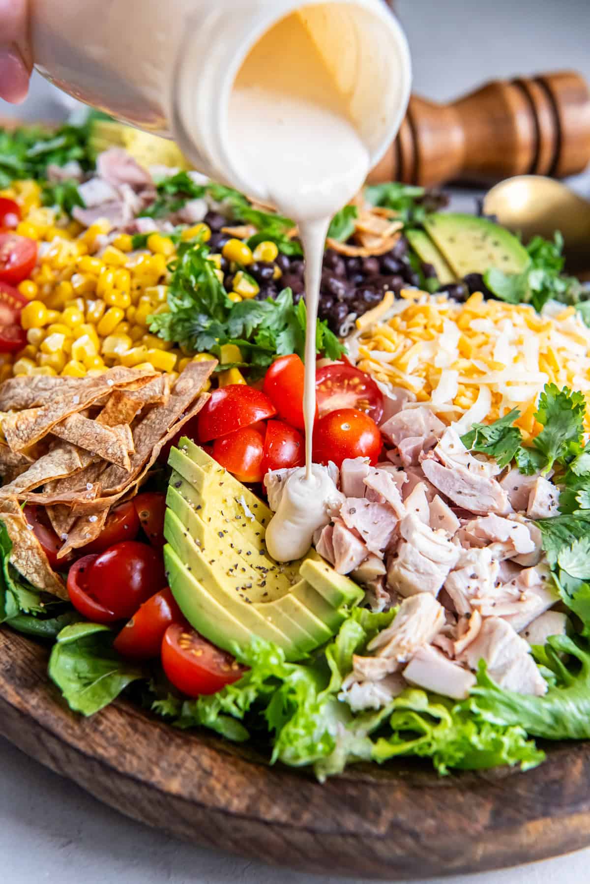 Creamy Caesar dressing being poured over a Southwest Chicken Caesar Salad with romaine, chicken, avocado, black beans, corn, tomatoes, shredded cheese, and crispy tortilla strips.