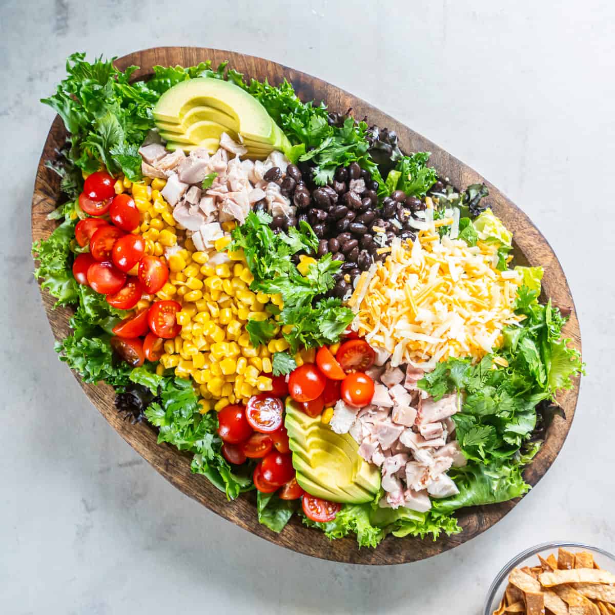 Ingredients for Southwest Chicken Caesar Salad arranged on a platter, including romaine, rotisserie chicken, black beans, corn, tomatoes, avocado, cheese, and cilantro.