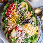 Southwest Chicken Caesar Salad drizzled with creamy Caesar dressing, topped with chicken, avocado, black beans, corn, tomatoes, shredded cheese, and crispy tortilla strips.