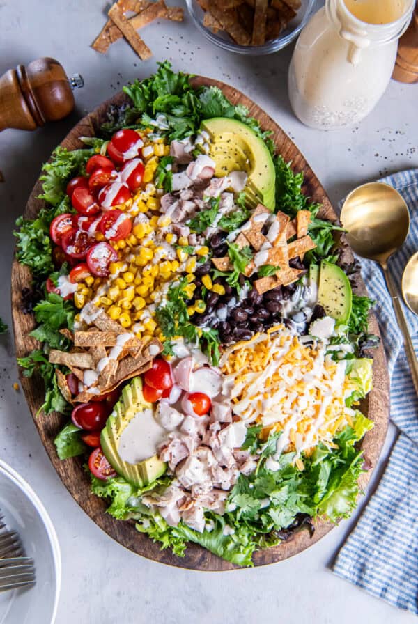 Southwest Chicken Caesar Salad drizzled with creamy Caesar dressing, topped with chicken, avocado, black beans, corn, tomatoes, shredded cheese, and crispy tortilla strips.