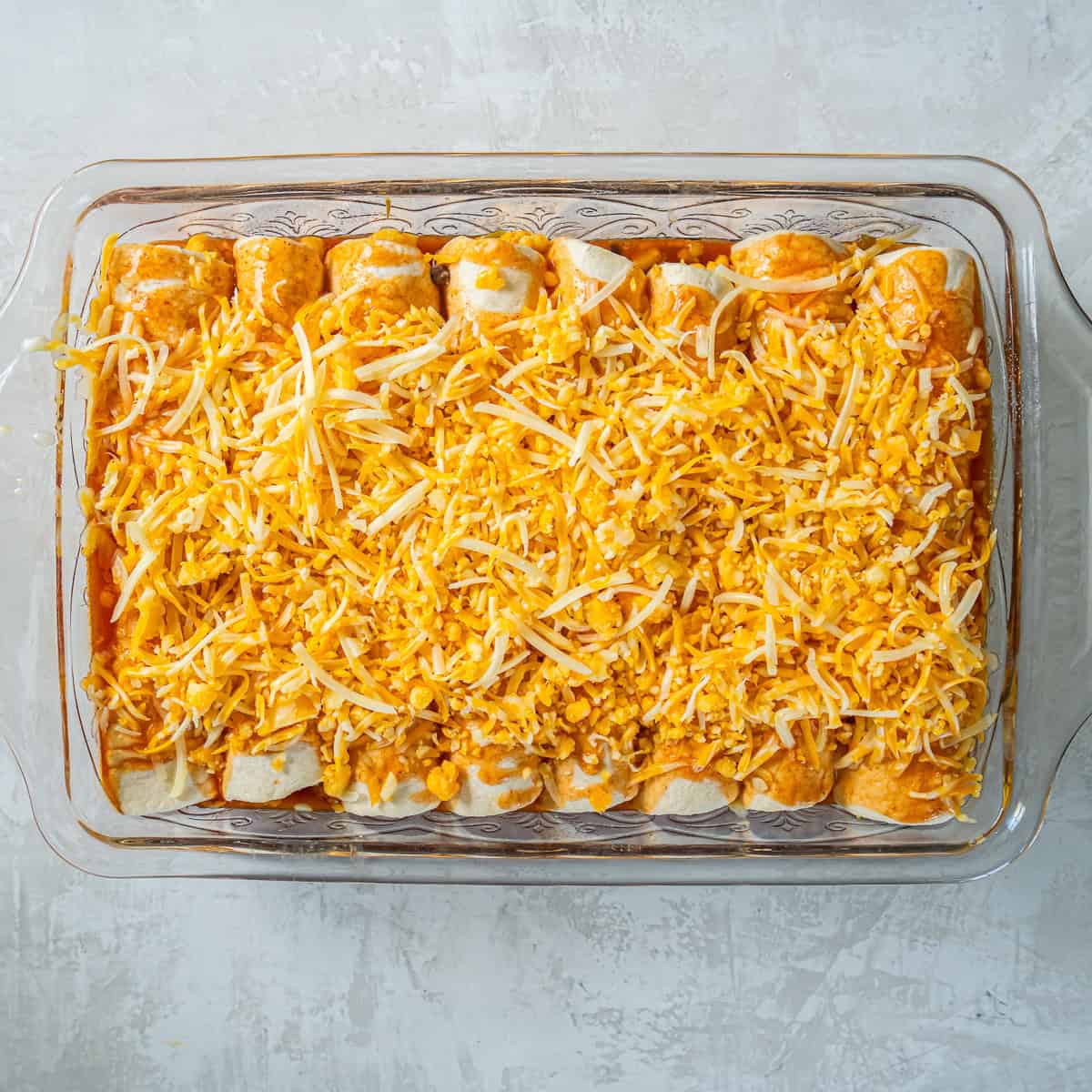 Chicken enchiladas topped with shredded Mexican blend cheese after the initial baking time.