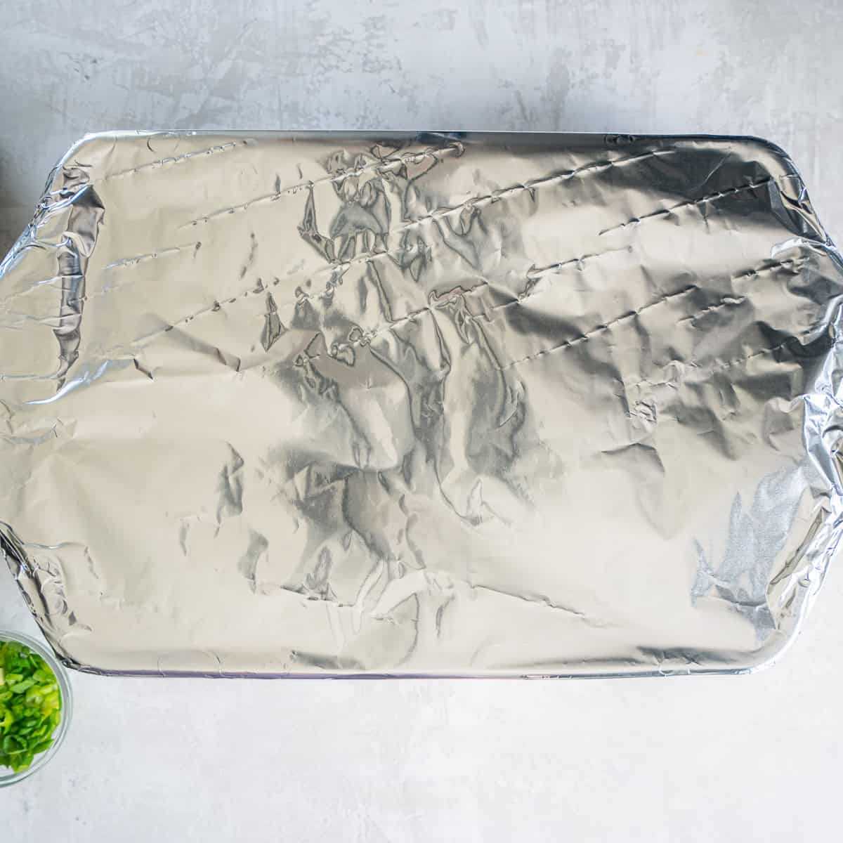 Baking dish of chicken enchiladas covered tightly with aluminum foil before baking.
