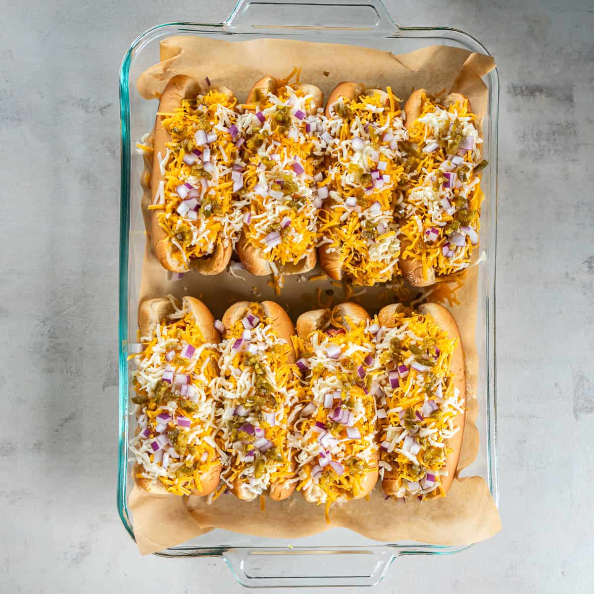 Chili dogs topped with shredded cheddar and Monterey Jack cheese, red onion, and pickled jalape&ntilde;os before baking.