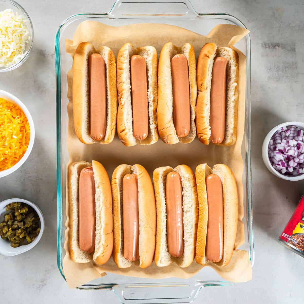 Eight hot dogs in buns arranged in a parchment-lined baking dish.