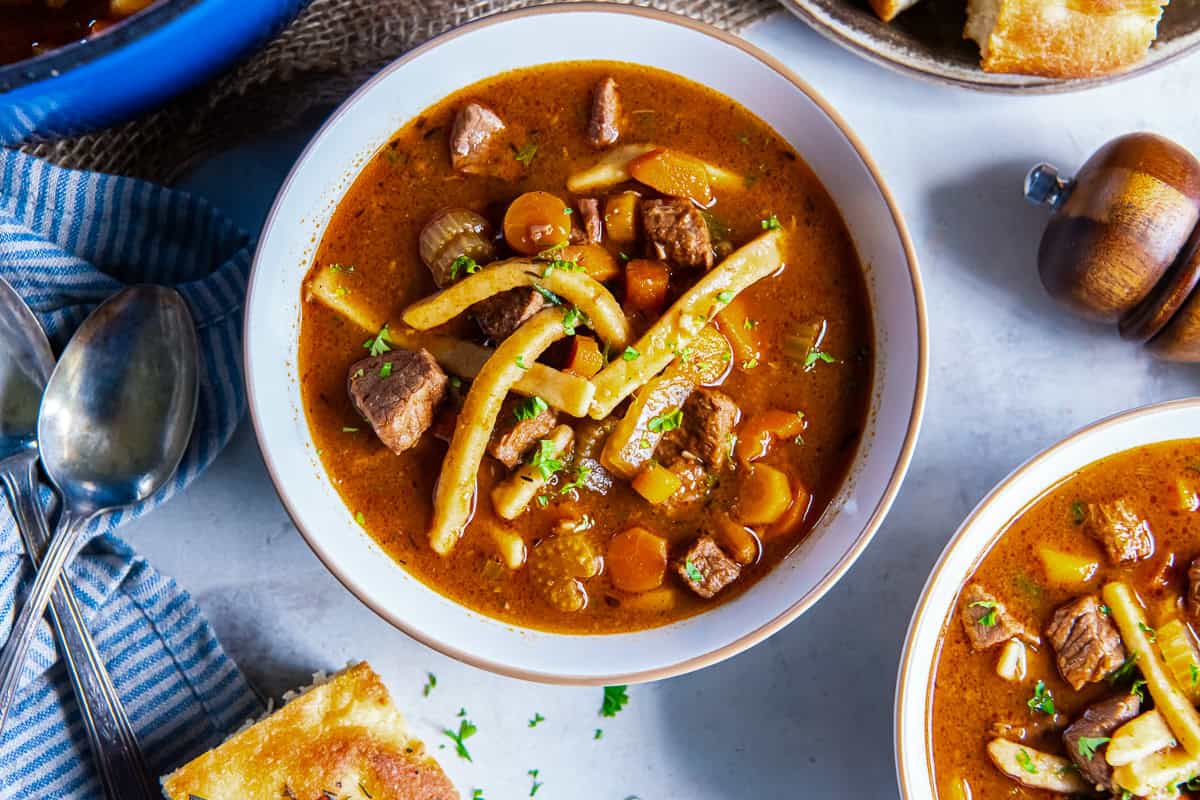Beef noodle soup with tender beef, egg noodles, carrots, and celery in a rich broth, served with focaccia bread.