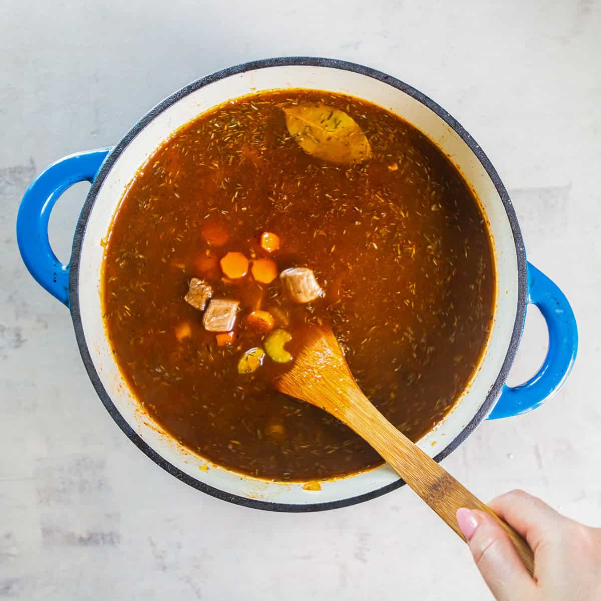 Beef and vegetables simmering in broth in a Dutch oven.