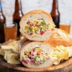 Chopped Italian Sandwich halves stacked on a wooden board, showing the creamy chopped deli meat, cheese, lettuce, tomato, pickles, and banana pepper filling.