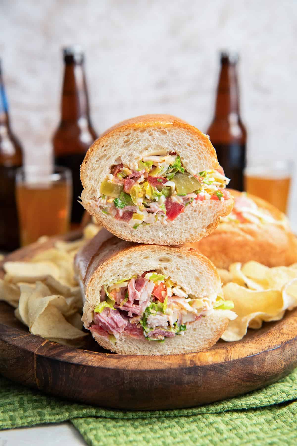 Chopped Italian Sandwich halves stacked on a wooden board, showing the creamy chopped deli meat, cheese, lettuce, tomato, pickles, and banana pepper filling.