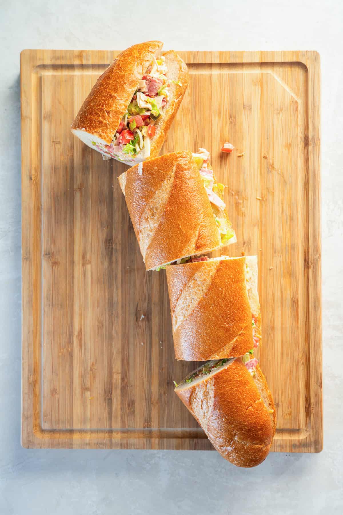 Sliced Chopped Italian Sandwich on a cutting board, showing layers of turkey, ham, salami, cheese, lettuce, tomato, pickles, banana peppers, and creamy ranch dressing.