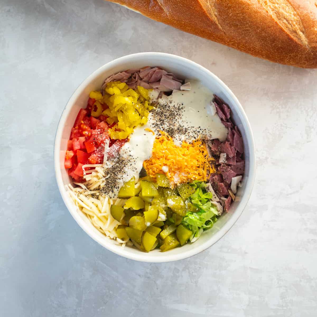 Chopped Italian sandwich ingredients in a bowl with turkey, ham, salami, romaine, tomato, cheeses, pickles, banana peppers, ranch, salt, and pepper.
