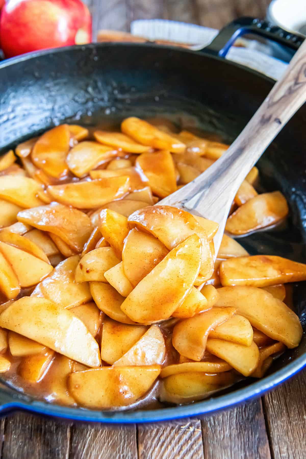 Cinnamon apples coated in a glossy brown sugar cinnamon sauce in a skillet with a wooden spoon.
