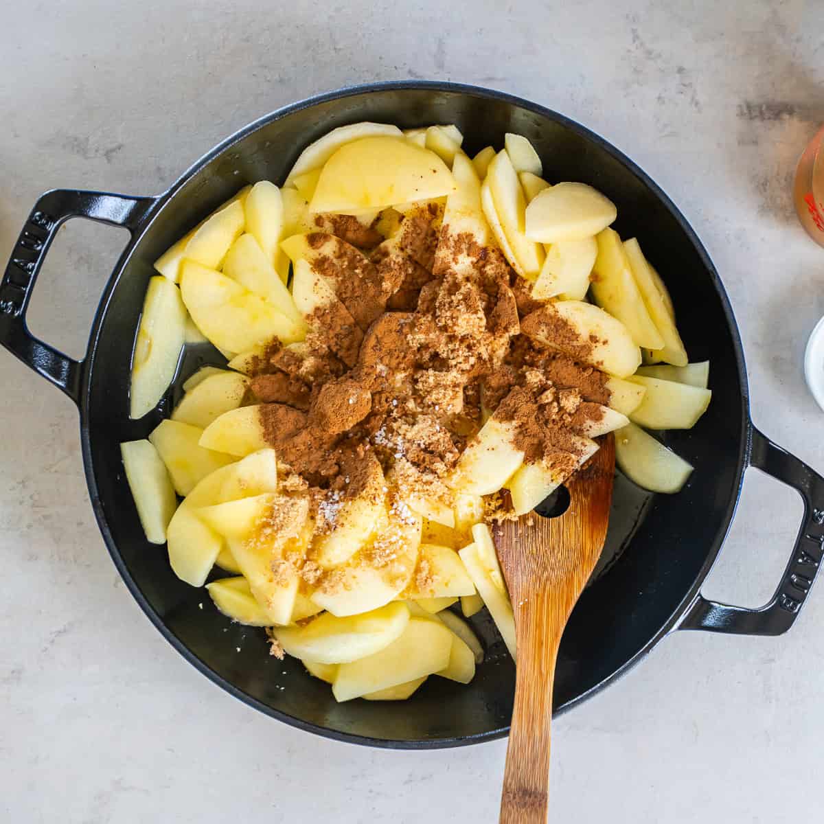 Sliced apples sprinkled with brown sugar, cinnamon, and salt in a skillet.