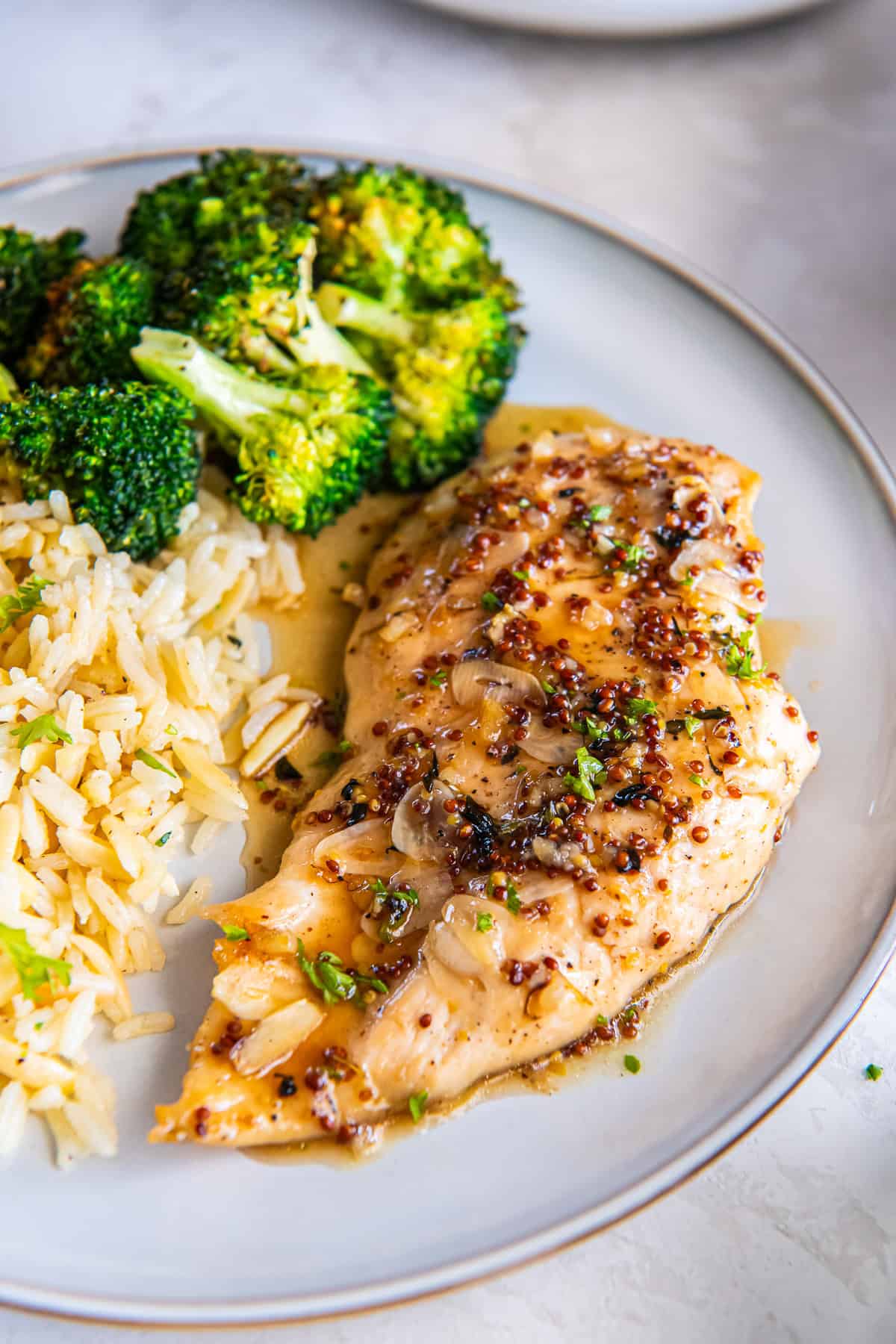 Maple mustard chicken breast with sliced garlic and sauce, served with rice and broccoli.