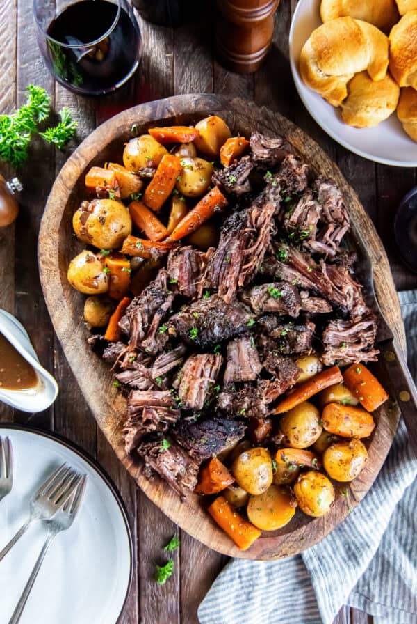 Tender slow cooker chuck roast with carrots and baby potatoes on a wooden serving platter, garnished with fresh parsley and served with gravy.