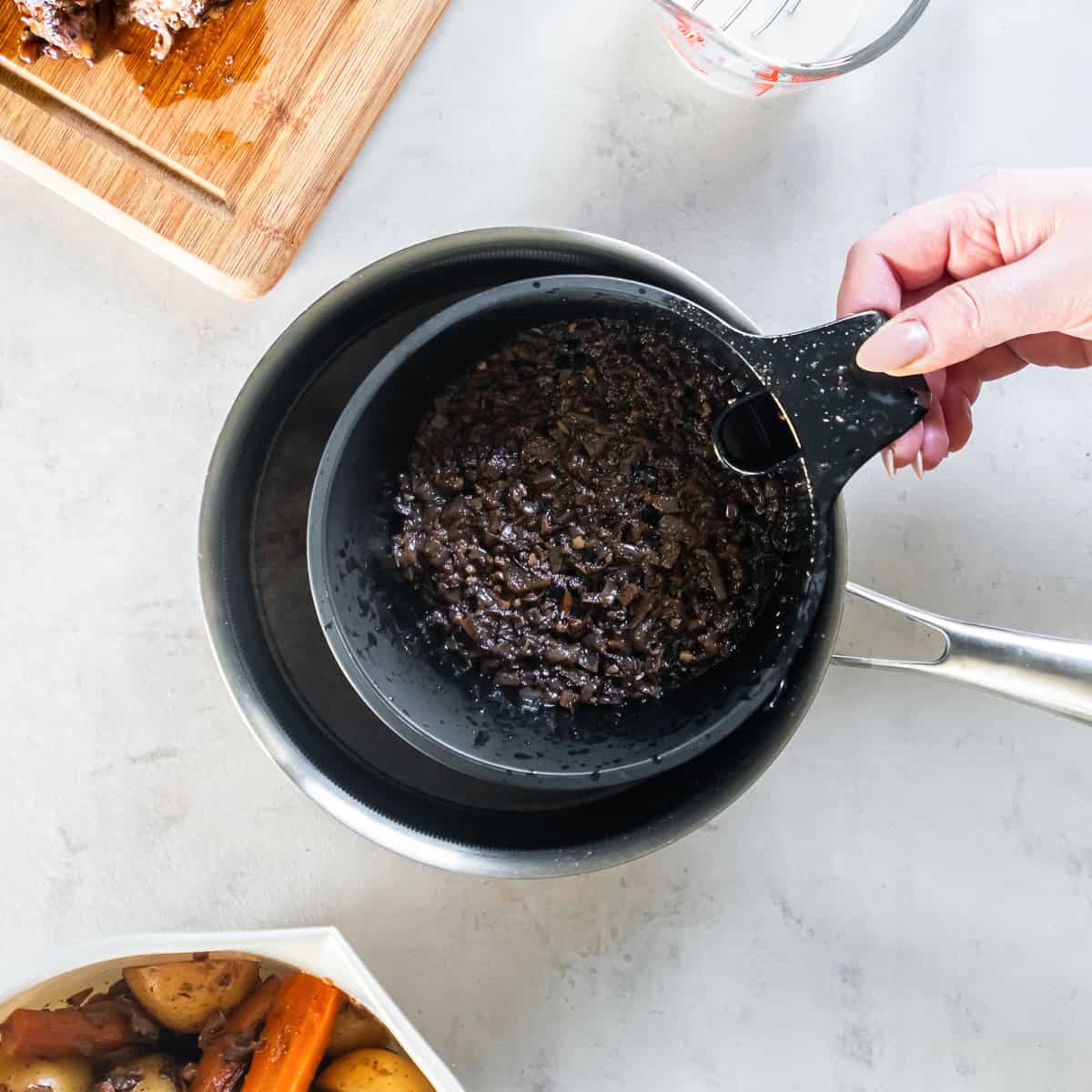 Straining slow cooker chuck roast drippings through a fine-mesh strainer to make homemade gravy.